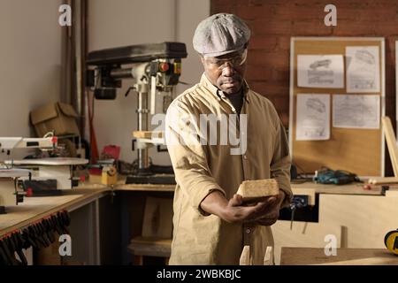 Afroamerikaner Senior-Mann als geschickter Zimmermann, der Holzbretter im Sonnenlicht inspiziert Stockfoto