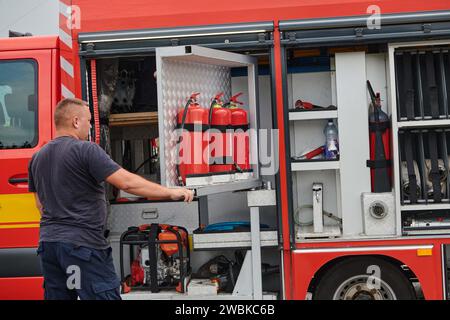 Ein dedizierter Feuerwehrmann bereitet einen modernen Feuerwehrwagen für den Einsatz in gefährdeten Bereichen vor, in denen ein Brand geschädigt wird, und demonstriert damit Bereitschaft und Engagement Stockfoto