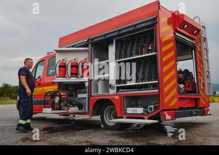 Ein dedizierter Feuerwehrmann bereitet einen modernen Feuerwehrwagen für den Einsatz in gefährdeten Bereichen vor, in denen ein Brand geschädigt wird, und demonstriert damit Bereitschaft und Engagement Stockfoto