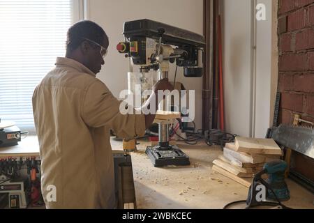 Schwarzer Zimmermann, der Holzschneidemaschinen in der Werkstatt benutzt und an einem Wohnungsprojekt arbeitet Stockfoto