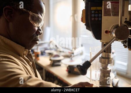 Seitliche Nahaufnahme des Schwarzen Mannes in Schutzbrille mit Werkzeugmaschinen in der Tischlerwerkstatt Stockfoto