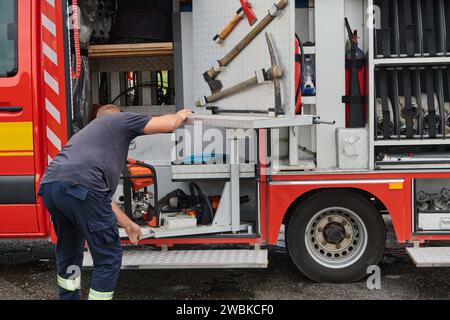 Ein dedizierter Feuerwehrmann bereitet einen modernen Feuerwehrwagen für den Einsatz in gefährdeten Bereichen vor, in denen ein Brand geschädigt wird, und demonstriert damit Bereitschaft und Engagement Stockfoto