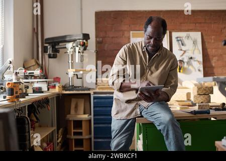 Porträt eines afroamerikanischen Seniorenmannes mit digitalem Tablet in einer kleinen Tischlerei Stockfoto