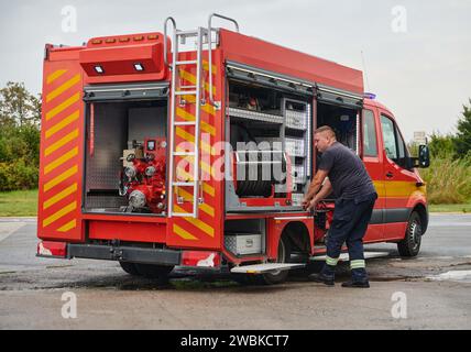 Ein dedizierter Feuerwehrmann bereitet einen modernen Feuerwehrwagen für den Einsatz in gefährdeten Bereichen vor, in denen ein Brand geschädigt wird, und demonstriert damit Bereitschaft und Engagement Stockfoto