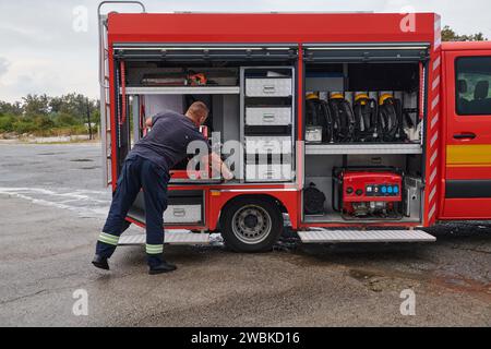 Ein dedizierter Feuerwehrmann bereitet einen modernen Feuerwehrwagen für den Einsatz in gefährdeten Bereichen vor, in denen ein Brand geschädigt wird, und demonstriert damit Bereitschaft und Engagement Stockfoto