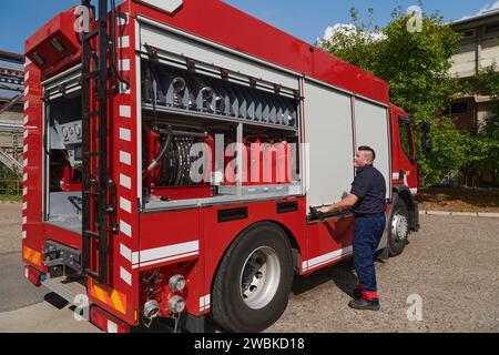 Ein dedizierter Feuerwehrmann bereitet einen modernen Feuerwehrwagen für den Einsatz in gefährdeten Bereichen vor, in denen ein Brand geschädigt wird, und demonstriert damit Bereitschaft und Engagement Stockfoto