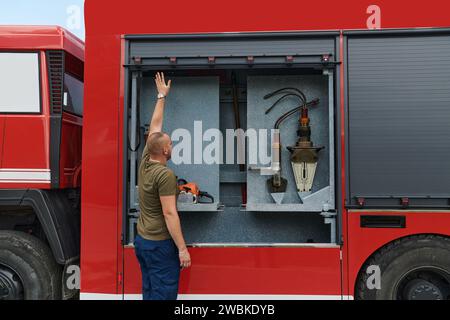 Ein dedizierter Feuerwehrmann bereitet einen modernen Feuerwehrwagen für den Einsatz in gefährdeten Bereichen vor, in denen ein Brand geschädigt wird, und demonstriert damit Bereitschaft und Engagement Stockfoto