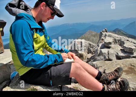 Wanderung zur Soiernspitze (2257 m), junger Mann macht einen Eintrag in das Gipfelbuch, vor einem hellblauen Himmel, Soierngruppe, Soiernberggruppe, Karwende Stockfoto