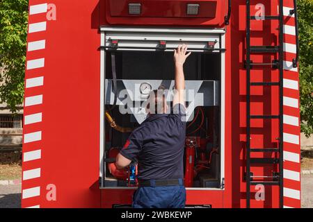 Ein dedizierter Feuerwehrmann bereitet einen modernen Feuerwehrwagen für den Einsatz in gefährdeten Bereichen vor, in denen ein Brand geschädigt wird, und demonstriert damit Bereitschaft und Engagement Stockfoto