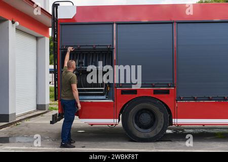 Ein dedizierter Feuerwehrmann bereitet einen modernen Feuerwehrwagen für den Einsatz in gefährdeten Bereichen vor, in denen ein Brand geschädigt wird, und demonstriert damit Bereitschaft und Engagement Stockfoto