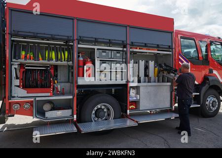 Ein dedizierter Feuerwehrmann bereitet einen modernen Feuerwehrwagen für den Einsatz in gefährdeten Bereichen vor, in denen ein Brand geschädigt wird, und demonstriert damit Bereitschaft und Engagement Stockfoto