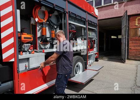 Ein dedizierter Feuerwehrmann bereitet einen modernen Feuerwehrwagen für den Einsatz in gefährdeten Bereichen vor, in denen ein Brand geschädigt wird, und demonstriert damit Bereitschaft und Engagement Stockfoto