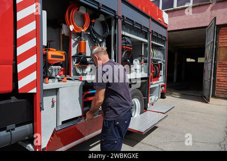 Ein dedizierter Feuerwehrmann bereitet einen modernen Feuerwehrwagen für den Einsatz in gefährdeten Bereichen vor, in denen ein Brand geschädigt wird, und demonstriert damit Bereitschaft und Engagement Stockfoto