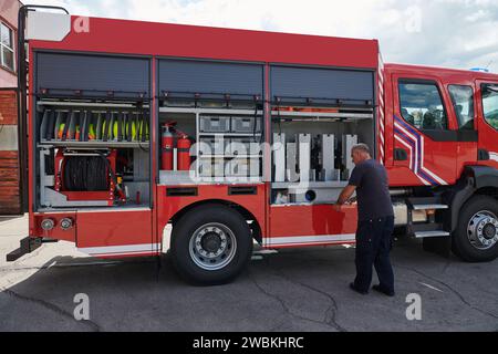 Ein dedizierter Feuerwehrmann bereitet einen modernen Feuerwehrwagen für den Einsatz in gefährdeten Bereichen vor, in denen ein Brand geschädigt wird, und demonstriert damit Bereitschaft und Engagement Stockfoto