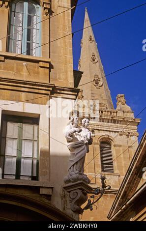 Jungfrau Maria mit Kinderstatue an einer Straßenecke und dem Turm der St. Paul Kathedrale über den Apartments in Valletta, Malta Stockfoto