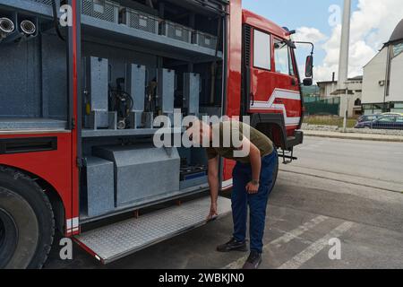 Ein dedizierter Feuerwehrmann bereitet einen modernen Feuerwehrwagen für den Einsatz in gefährdeten Bereichen vor, in denen ein Brand geschädigt wird, und demonstriert damit Bereitschaft und Engagement Stockfoto