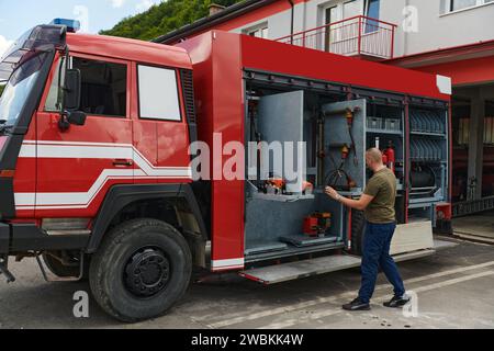 Ein dedizierter Feuerwehrmann bereitet einen modernen Feuerwehrwagen für den Einsatz in gefährdeten Bereichen vor, in denen ein Brand geschädigt wird, und demonstriert damit Bereitschaft und Engagement Stockfoto