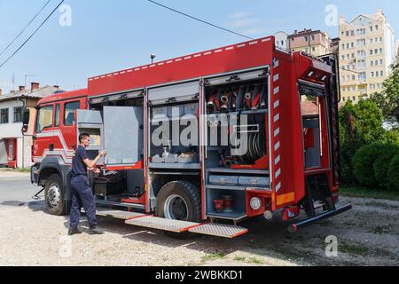 Ein dedizierter Feuerwehrmann bereitet einen modernen Feuerwehrwagen für den Einsatz in gefährdeten Bereichen vor, in denen ein Brand geschädigt wird, und demonstriert damit Bereitschaft und Engagement Stockfoto