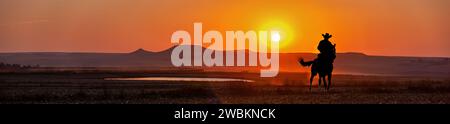 Silhouette Cowboy bei Sonnenuntergang reiten in der Nähe eines Wasserlochs in der Prärie, blick auf die Landschaft des amerikanischen Westens Stockfoto