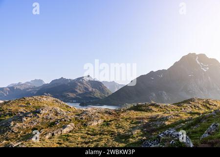 Die Sonne strahlt ein goldenes Licht über eine zerklüftete Landschaft und hebt das strukturierte Gelände und die fernen Berge in Lofoten, Norwegen, hervor Stockfoto