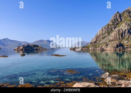 Das ruhige Wasser des Norwegischen Meeres trifft sanft auf die felsige Küste der Lofoten, mit majestätischen Bergen, die sich im klaren Wasser spiegeln Stockfoto