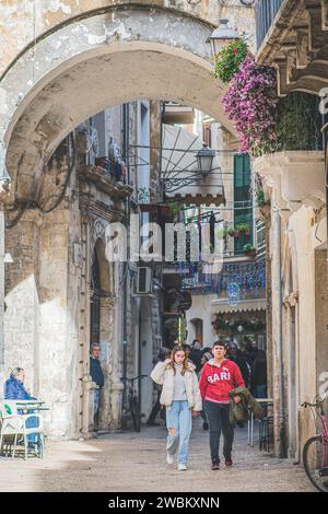 Enge Straße mit Touristen, die unter einem Bogen in der Altstadt von Bari laufen, Apulien, Italien, vertikal Stockfoto