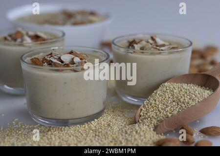 Köstlicher Proso Millet Kheer in einer Glasschale, geschmückt mit knusprigen Mandeln, mit einem nahrhaften Dessert. Um die Schüssel herum ist ein großzügiger Haufen Stockfoto