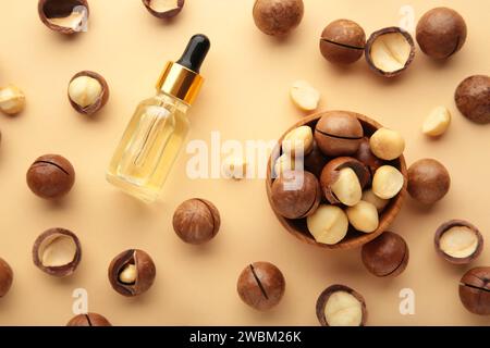 Geschälte Macadamia-Nüsse in einer Holzschale mit Öl auf beigem Hintergrund. Draufsicht Stockfoto