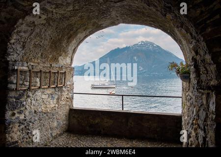 Das Segelboot legte im Winter in Varenna an, eingerahmt von einem bogenförmigen Steinfenster. Berge in der Ferne, Comer See, Varenna, Seenregion, Lombardei, Stockfoto