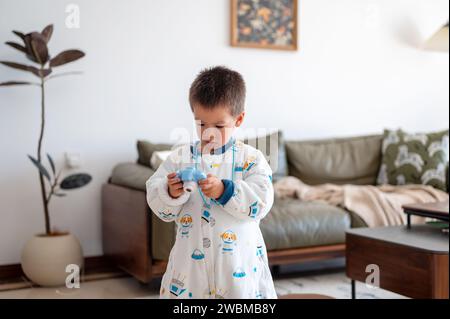 Charmanter zweieinhalb Jahre kleiner Junge, der Spaß beim Spielen und Fotografieren mit einer digitalen Kinderkamera im Wohnzimmer zu Hause hat Stockfoto