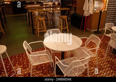 Ein Set aus vier weißen Plastikstühlen auf einem weißen rechteckigen Tisch, in einer ordentlichen Reihe angeordnet Stockfoto
