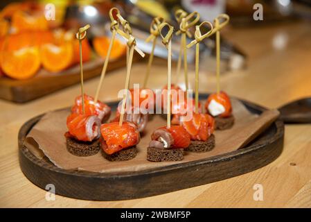 Elegante Räucherlachskanapees mit Frischkäse auf dunklen Roggenbrotstücken, präsentiert auf einer hölzernen Servierplatte. Stockfoto