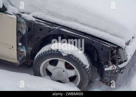 Altes zertrümmertes Auto, bedeckt mit Schnee. Fragment eines verlassenen alten Autos im Schnee. Stockfoto