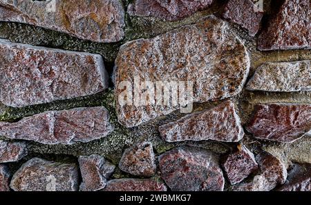 Wand aus großen Steinen. Abstrakter Hintergrund von der Oberfläche der mit Frost bedeckten Steine. Stockfoto