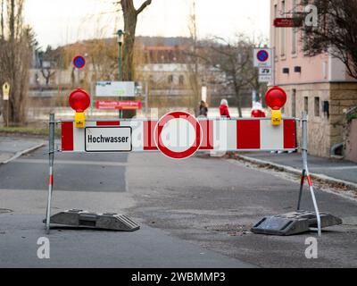 Hochwasser-Schild an einer Barriere. Die Straße ist wegen möglicher Gefahr gesperrt. Ein Fluss hat hohe Wasserstände und verursacht Schäden. Stockfoto