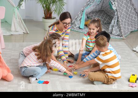 Kleine Kinder mit Kindergärtnerin beim Puzzle im Kindergarten Stockfoto