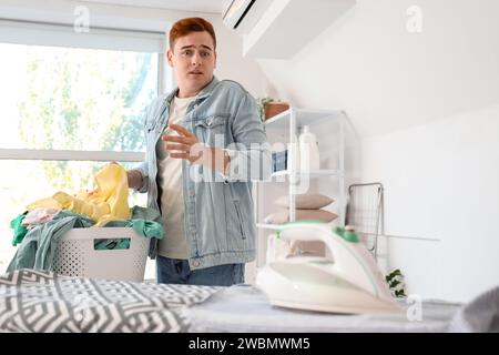 Der in Panik geratene junge Mann vergaß, das elektrische Bügeleisen auf dem Hemd in der Wäscherei auszuschalten Stockfoto