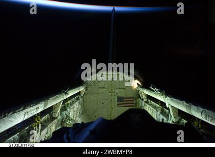 S133-E-011762 (7. März 2011) --- der vertikale Stabilisator des Space Shuttle Discovery, die Pods des Orbitalmanövriersystems (OMS), der Andockmechanismus, das Fernmanipulatorsystem/das Orbiter-Auslegersensorsystem (RMS/OBSS) und die Nutzladestelle sind in diesem Bild zu sehen, das von einem STS-133-Besatzungsmitglied während der Aktivitäten am 12. Flugabt aufgenommen wurde. Die dünne Linie der Erdatmosphäre liegt oben. Stockfoto