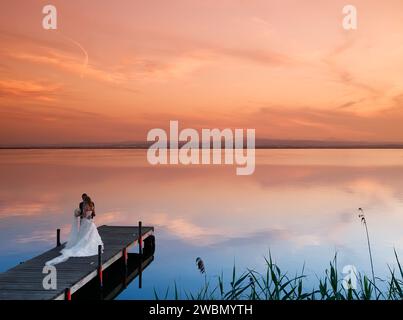 Frisch vermähltes Paar auf einer Strandpromenade am See mit einem traumhaften Sonnenuntergang mit wunderbaren Farben in Albufera, Valencia, Spanien Stockfoto