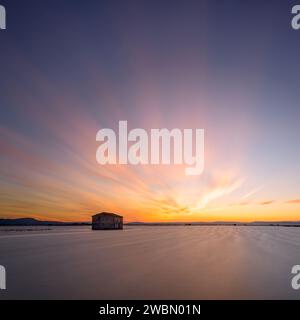 Wunderschöner Sonnenuntergang auf den überfluteten Reisfeldern mit einer Hütte Sonne versteckt sich am Horizont und alle Farben spiegeln sich im Wasser, Sueca, Valencia, Spanien Stockfoto