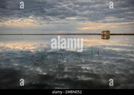 Wunderschöner Sonnenuntergang auf den überfluteten Reisfeldern mit einer Hütte Sonne versteckt sich am Horizont und alle Farben spiegeln sich im Wasser, Sueca, Valencia, Spanien Stockfoto