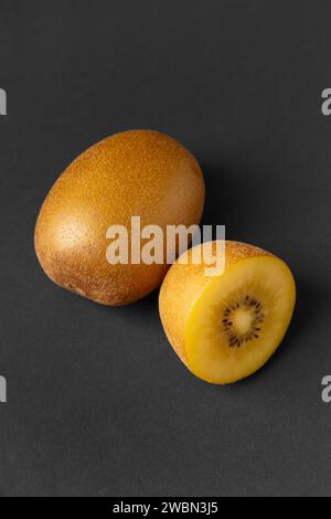 Ganze und halbierte reife goldene Kiwi, isoliert auf schwarzem Hintergrund. Kiwi mit gelb saftigem süßem Fruchtfleisch (Actinidia chinensis). Stockfoto