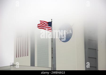 CAPE CANAVERAL, Fla. – Im Kennedy Space Center der NASA in Florida fliegt eine US-Flagge in der Nähe des 525 Meter hohen Vehicle Assembly Building, das im Nebel verdeckt ist. Das riesige Gebäude, das einst für die Verarbeitung von Apollo Saturn V-Raketen und Space Shuttles für den Start genutzt wurde, durchläuft derzeit eine Transformation, um es für die nächste Generation der NASA-Rakete, das Space Launch System oder SLS, sowie für unzählige kommerzielle Raketen in Entwicklung vorzubereiten. Stockfoto