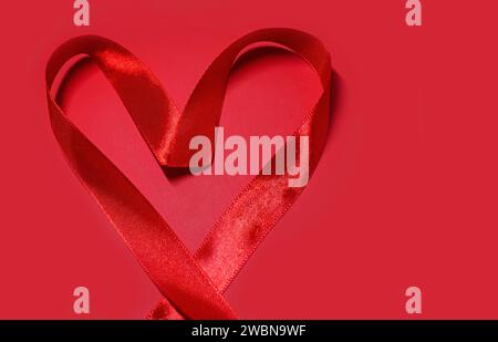 Rote Herzform vom Satinband Valentinstag auf rotem Hintergrund mit Kopierraum. Konzept für Wohltätigkeit, Krankenversicherung, Liebe, internationales Kardiolo Stockfoto