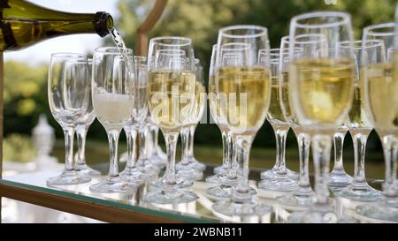 Champagner wird bei einer Dinnerparty verschüttet. Der Kellner schenkt Champagner. Catering bei der Veranstaltung. Ein Kellner gießt Champagner und Gläser in die Begrüßung im Freien Stockfoto