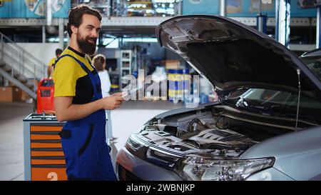 Porträt eines lizenzierten Technikers in der Autowerkstatt, der Routinekontrollen mit dem Tablet durchführt und auf Schäden achtet. Zertifizierter Mechaniker in der Werkstatt, der prüft, ob Fahrzeugkomponenten ausgetauscht werden müssen Stockfoto