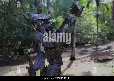 Lebensgroße Bronzeskulptur eines kleinen Mädchens mit Tauben auf dem Kopf und den Händen in den Na Aina Kai Botanical Gardens and Sculpture Park in Kilauea, Kauai, Stockfoto