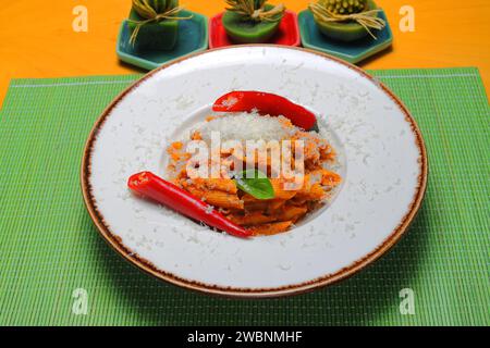Pene alla arrabiata, italienische Pasta mit roter Sauce, serviert auf einem Tisch auf einem Teller mit frisch geriebenem Parmesan. Stockfoto