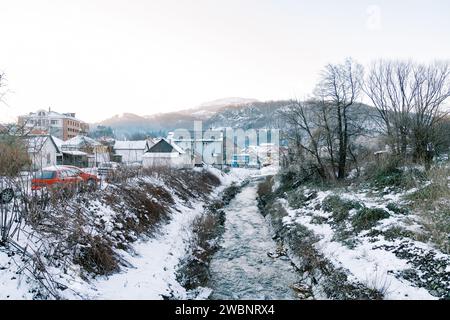 Der Gebirgsfluss fließt zwischen den schneebedeckten Ufern eines Dorfes am Fuße der Berge Stockfoto