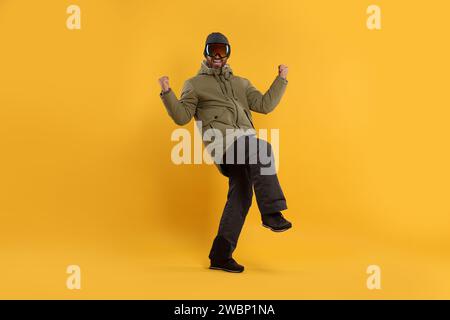 Wintersport. Fröhlicher Mann in Skianzug und Brille auf orangem Hintergrund Stockfoto